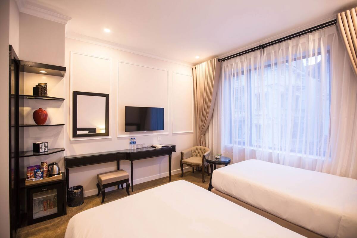 A hotel room with two beds, a desk with a TV, a chair, and a window with curtains.