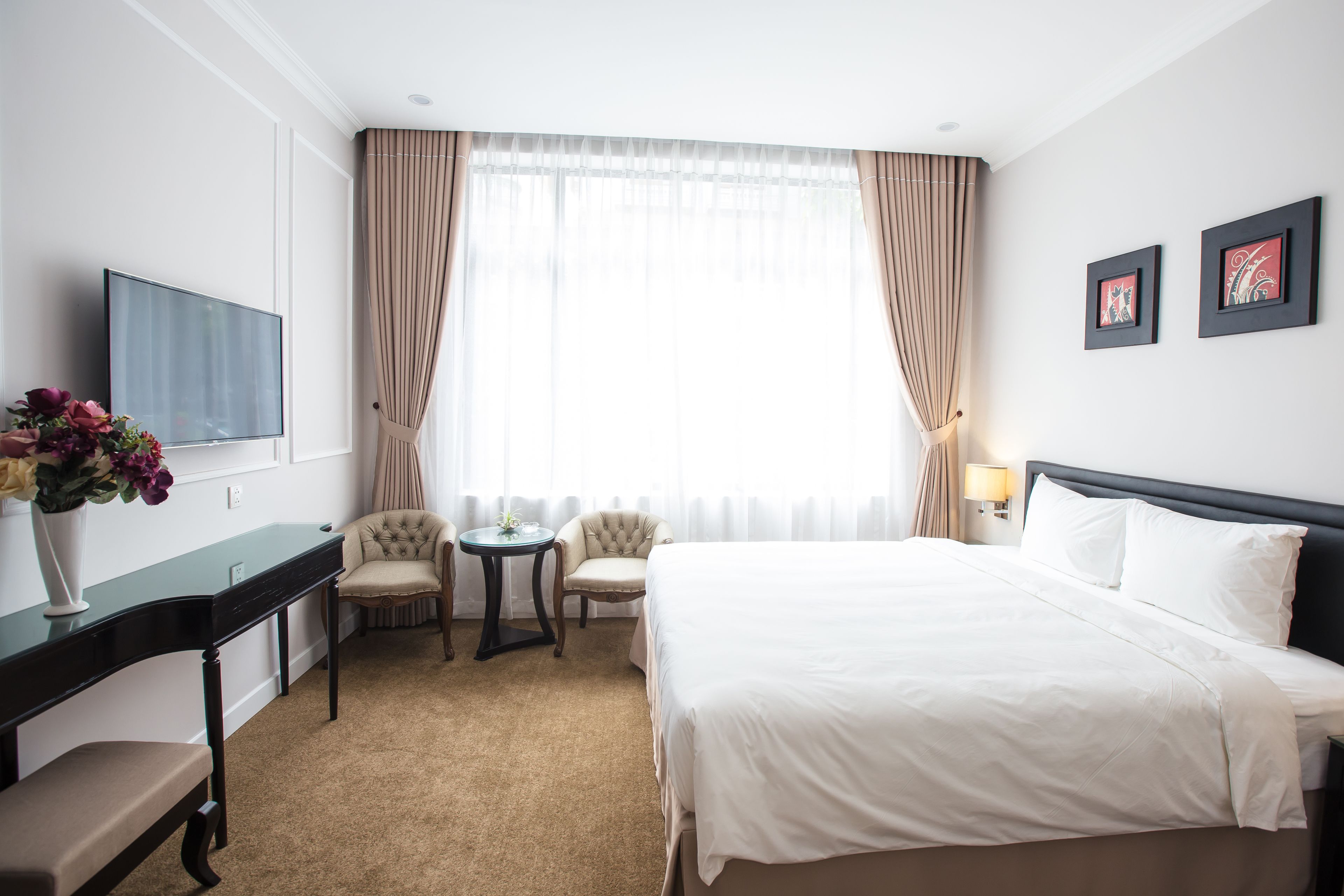 A hotel room with a large bed, a desk with a chair, a small round table, and two armchairs.