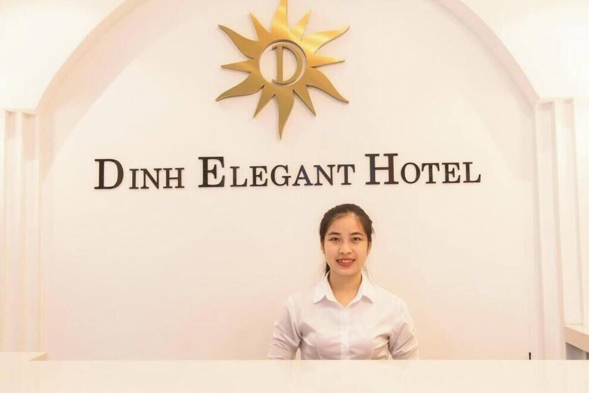 A reception desk with a sign that reads 'Dinh Elegant Hotel' and a sun emblem above it.
