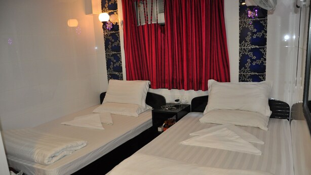 A hotel room with two single beds, a nightstand, and a window with red curtains. - New Guangzhou Guesthouse - Hostel (Kowloon)