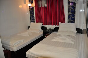 Una habitación de hotel con dos camas individuales, una mesita de noche y una ventana con cortinas rojas.