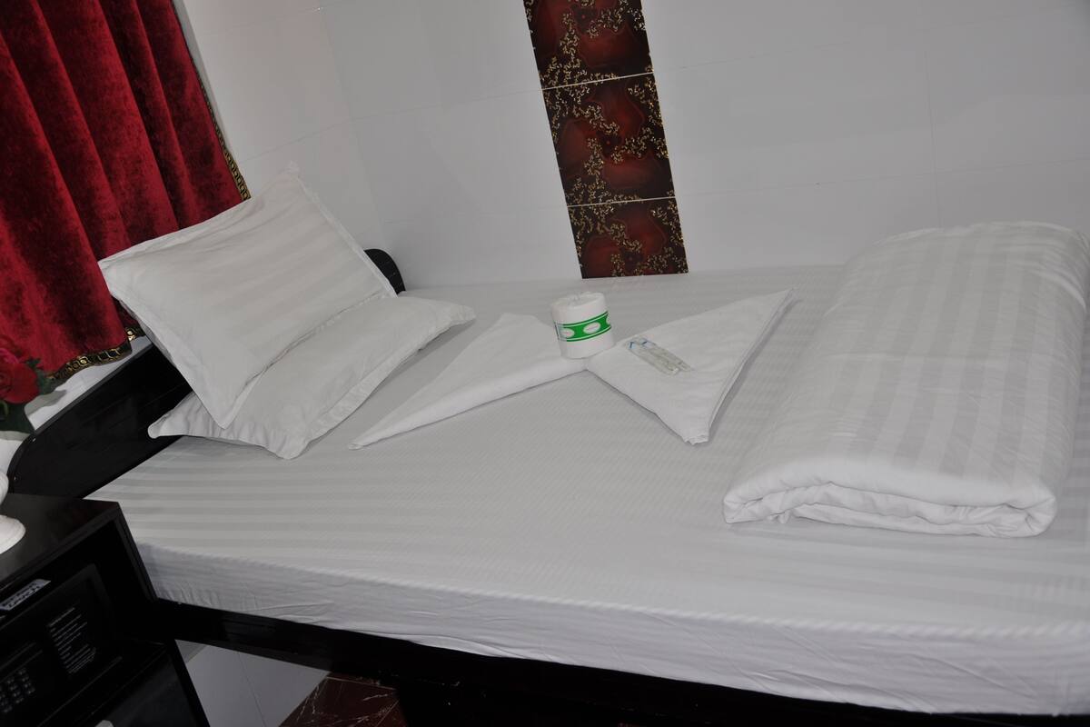 A neatly made bed with white linens, a pillow, a folded towel, and a small white container on the bed.