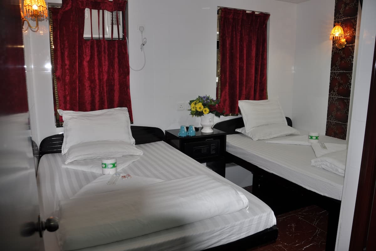 A hotel room with two single beds, a nightstand with a vase of flowers, and a mirror.