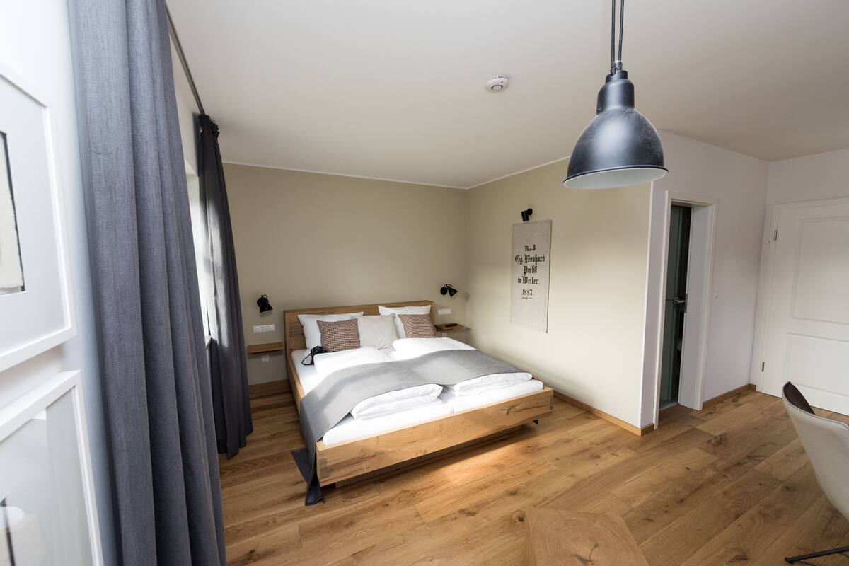 Une chambre à coucher avec un lit en bois, une lampe suspendue et une porte donnant sur une autre pièce.