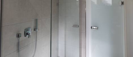 Ein modernes Badezimmer mit Duschkabine aus Glas, Handbrause und am Wand befestigtem Wasserhahn.