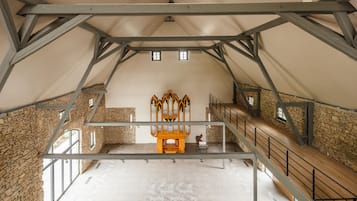 An attic room with exposed wooden beams, stone walls, and a wooden organ.