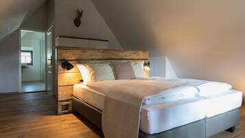 A bedroom with a sloped ceiling, a wooden headboard, a large bed with multiple pillows, and a small bench.