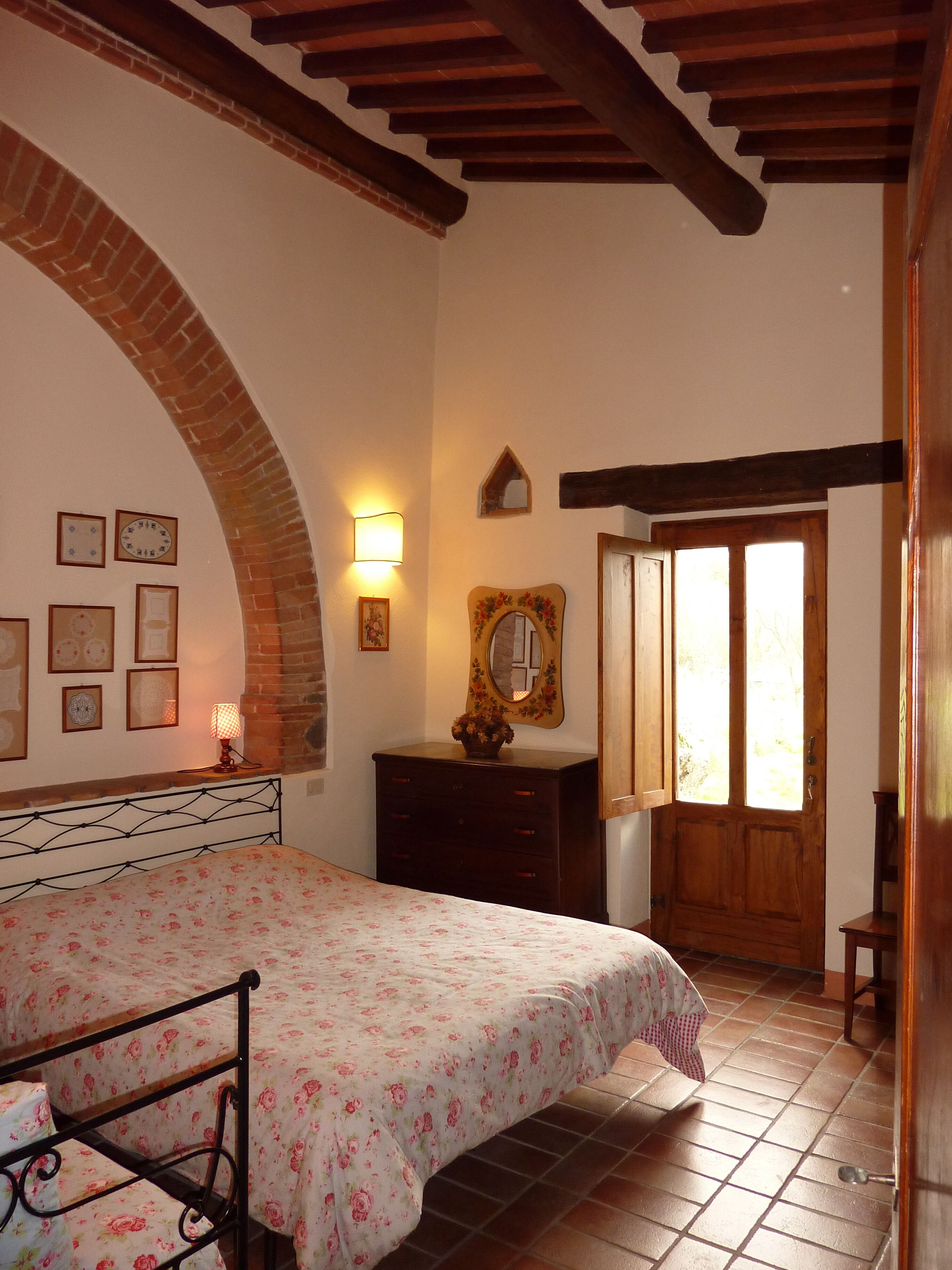 Ein Schlafzimmer mit Bett, Kommode und einer zur Außenseite führenden Tür.