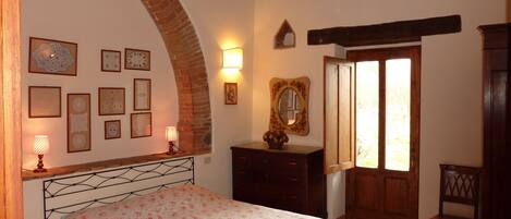 Un dormitori amb un llit, una petita taula de nit, un mirall i una porta amb finestreta.