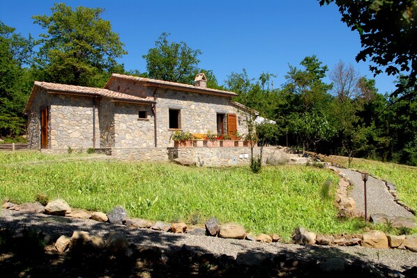 A stone house with a tiled roof, a small porch, and a gravel pathway leading to it. - Podere Pietreta (Radicofani)