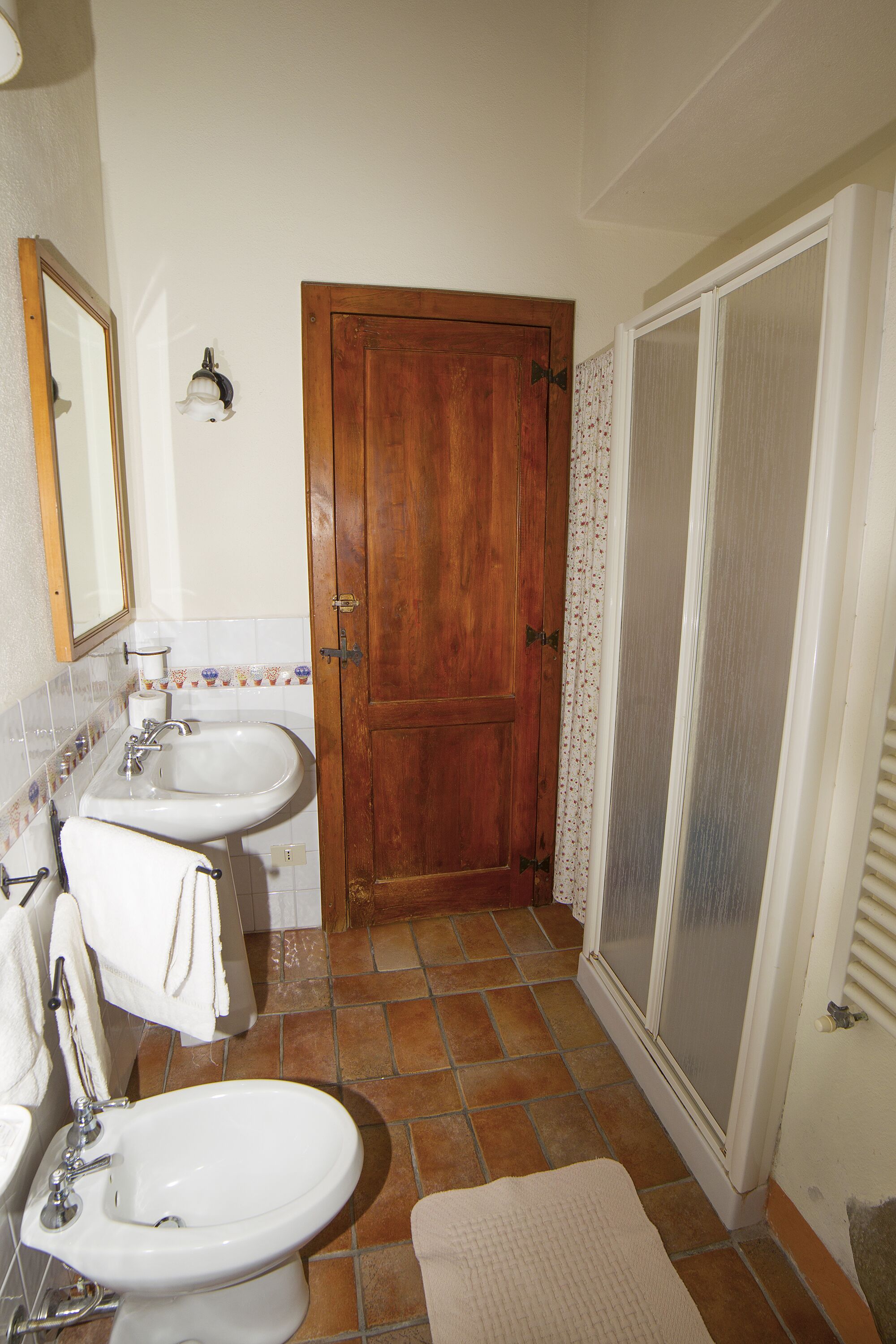 Une salle de bain avec une porte en bois, une douche avec une porte en verre et un lavabo avec un miroir.