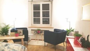 A compact living space with a sofa, a small table, and a window with blinds.