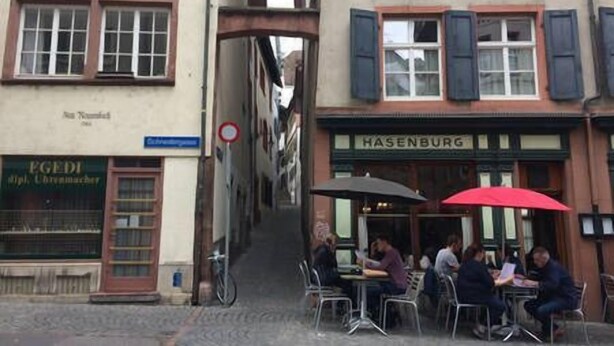 A narrow street with buildings on either side, a café with outdoor seating, and a bicycle parked on the sidewalk.