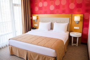 Een hotelkamer met een bed, twee nachtkastjes, een lamp en een raam met gordijnen.