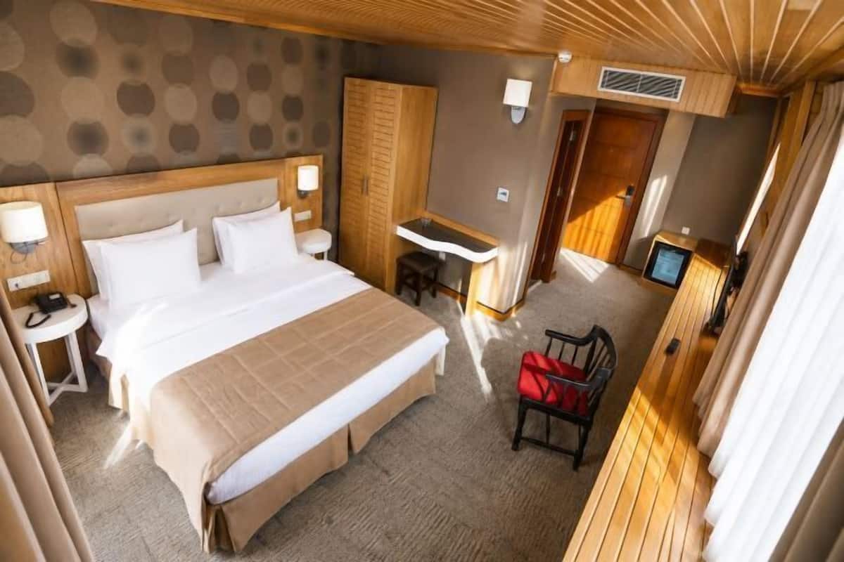A hotel room with a bed, desk, chair, TV, and a wardrobe.