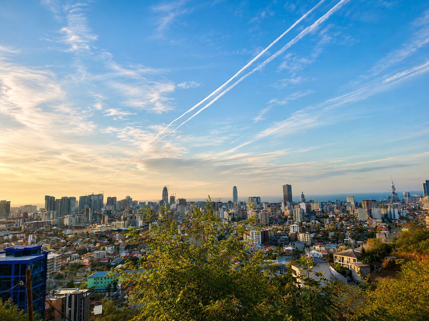 Un paisaje urbano con rascacielos, cielo despejado y estelas de condensación.
