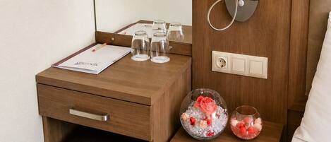 A hotel room with a wooden desk, a bedside table with a lamp, a chair, and a bed.