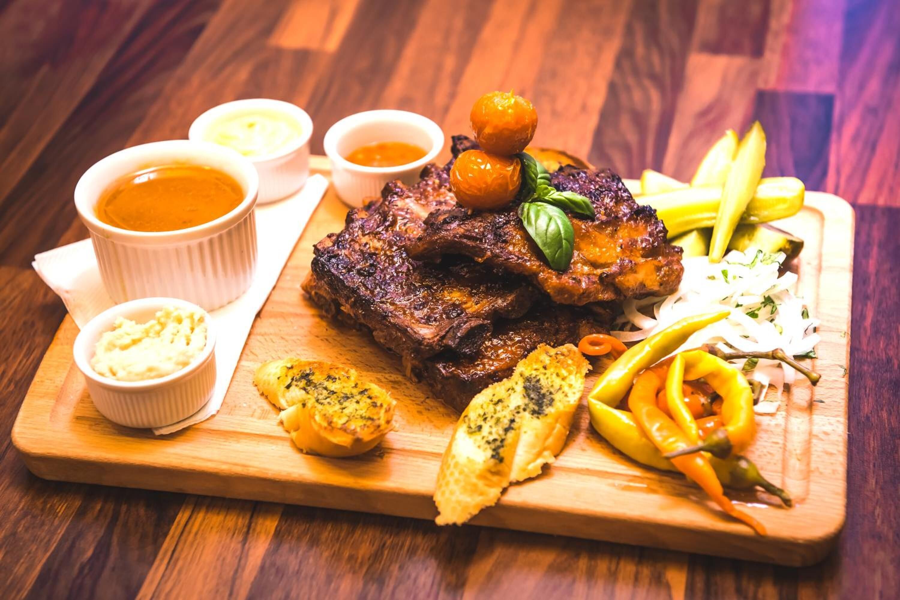 A wooden cutting board with grilled meat, pickles, and a side salad.