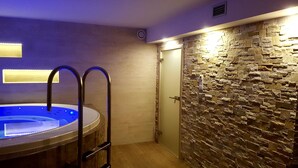A modern bathroom with a stone wall, a wooden floor, and a bathtub with a ladder. - Penzion Pepovka (Bela pod Pradedem)
