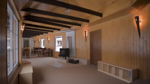A spacious room with wooden walls and a high ceiling. There is a fireplace, a dining table, and a sofa. - Penzion Pepovka (Bela pod Pradedem)