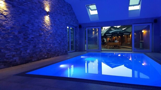 An indoor swimming pool with a glass wall and skylights, a brick wall, and a visible restaurant in the background. - Penzion Pepovka (Bela pod Pradedem)