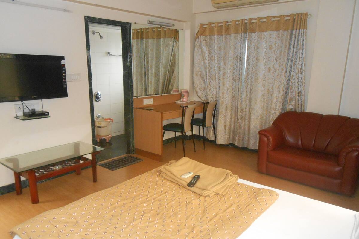 A hotel room with a bed, a desk, a television, a leather sofa, and a shower area.