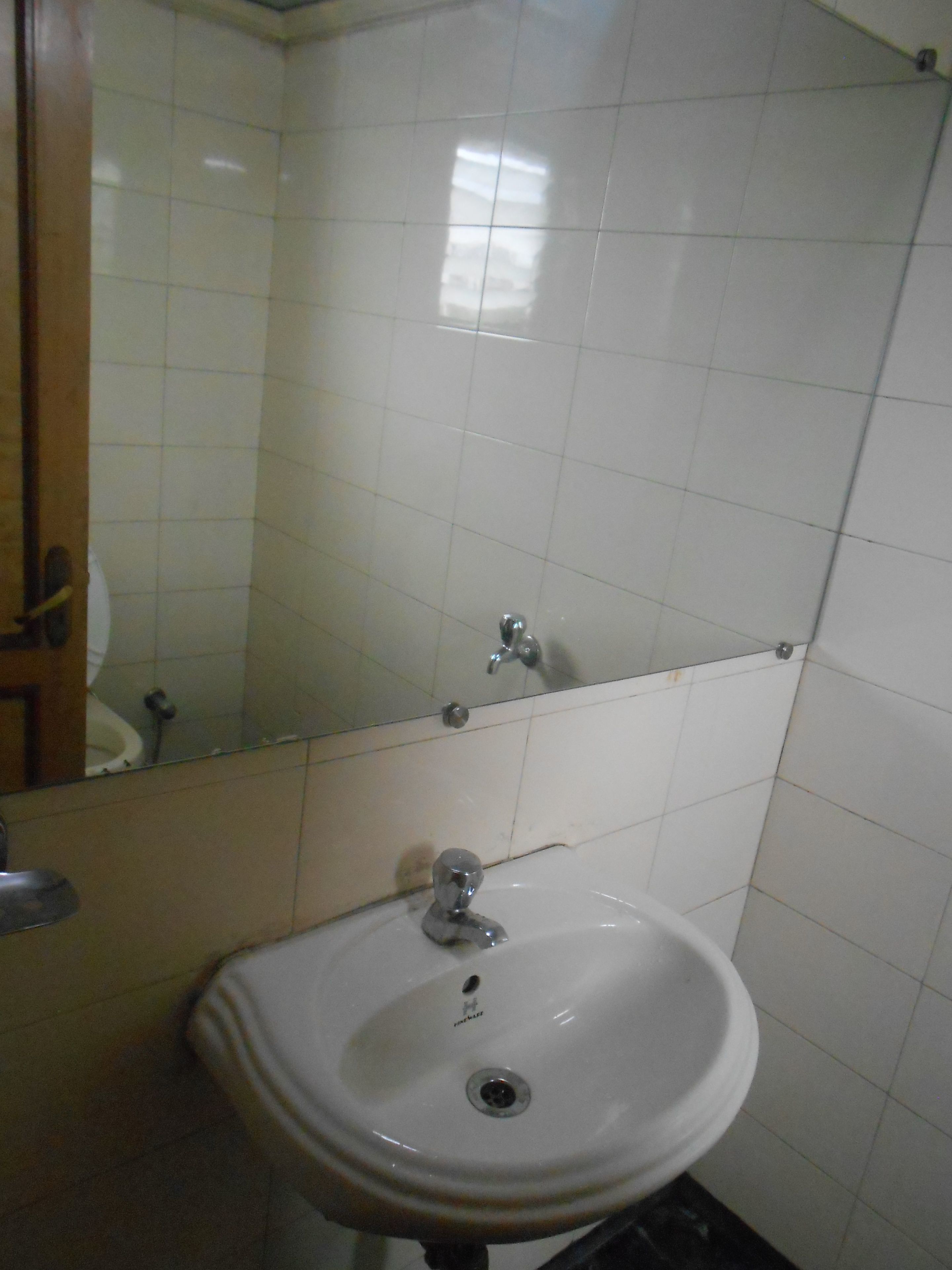 Un baño con lavamanos blanco, espejo y pared con azulejos.