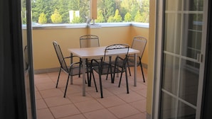 A balcony with a table and chairs, a view of trees, and a building in the background. - Appartement Vanii (Rust)