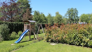 A playground with a slide and swings, surrounded by lush greenery and a bus in the background. - Appartement Vanii (Rust)
