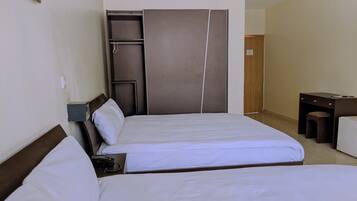 A hotel room with two beds, a desk, a wardrobe, and a small stool.