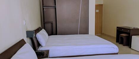 Et hotelværelse med to senge, et skrivebord, et klædeskab og en lille skammel.