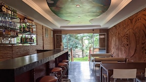 A bar area with stools, a counter with bottles, and a view of greenery outside. - Hotel Ruch (Kampala)