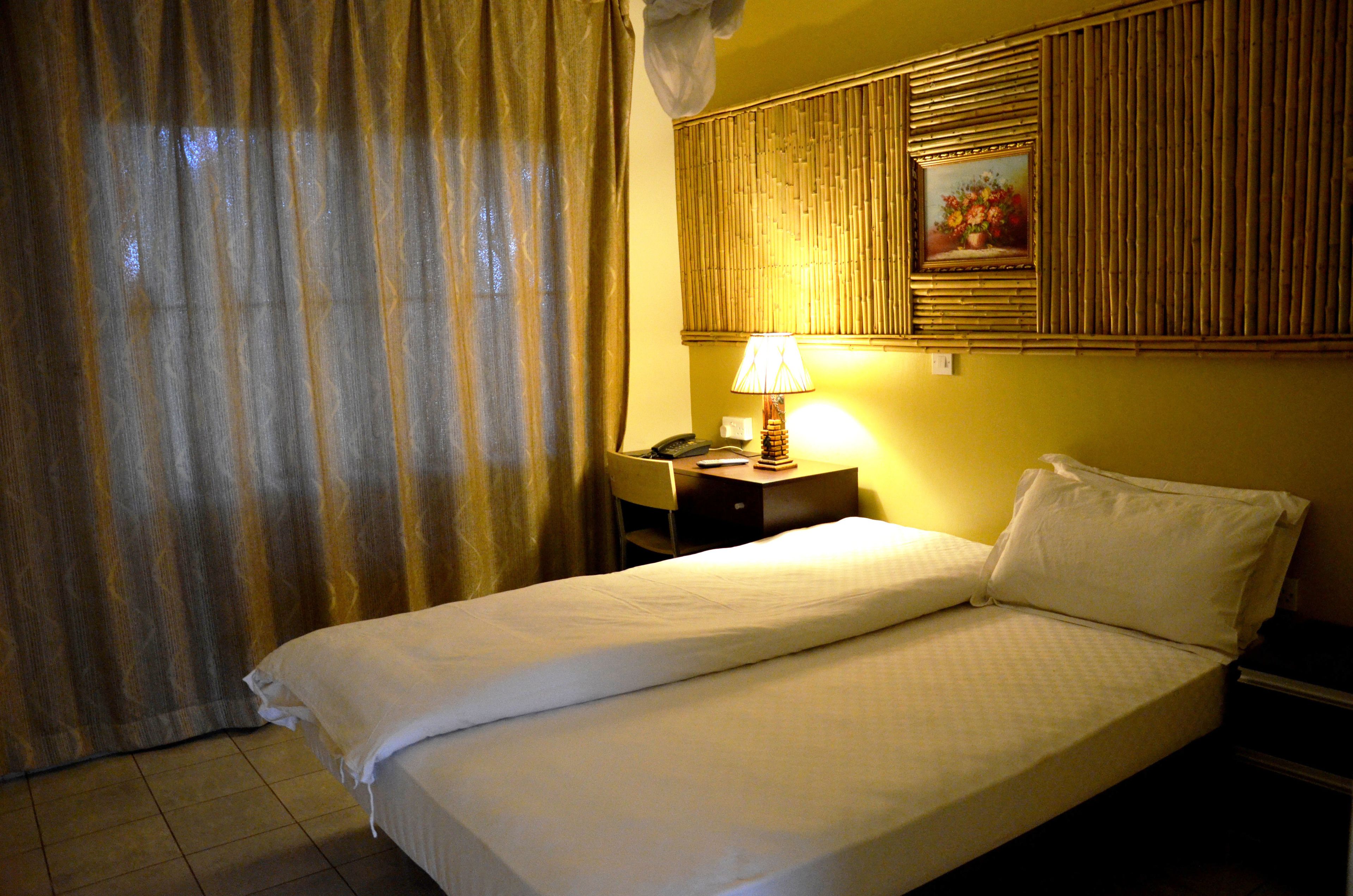 A hotel room with a bed, a desk, a lamp, and a painting on the wall.