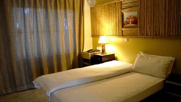 A hotel room with a bed, a desk, a lamp, and a painting on the wall.