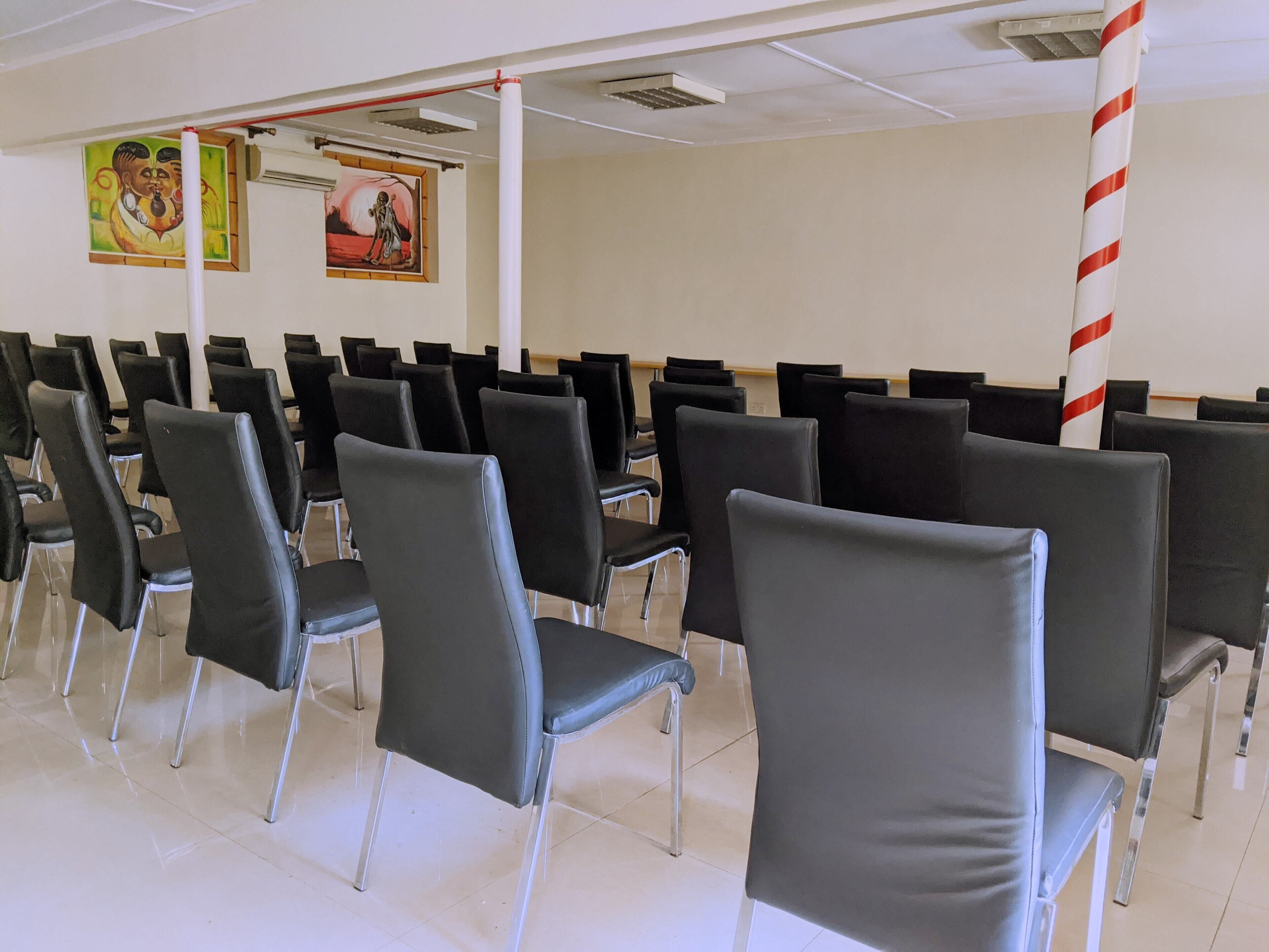Une salle d’attente avec des rangées de chaises noires et un pilier blanc orné de rayures rouges.