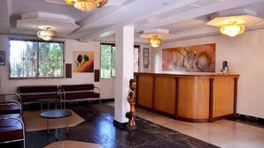 A reception area with a wooden desk, a bench, and a statue. - Hotel Ruch (Kampala)
