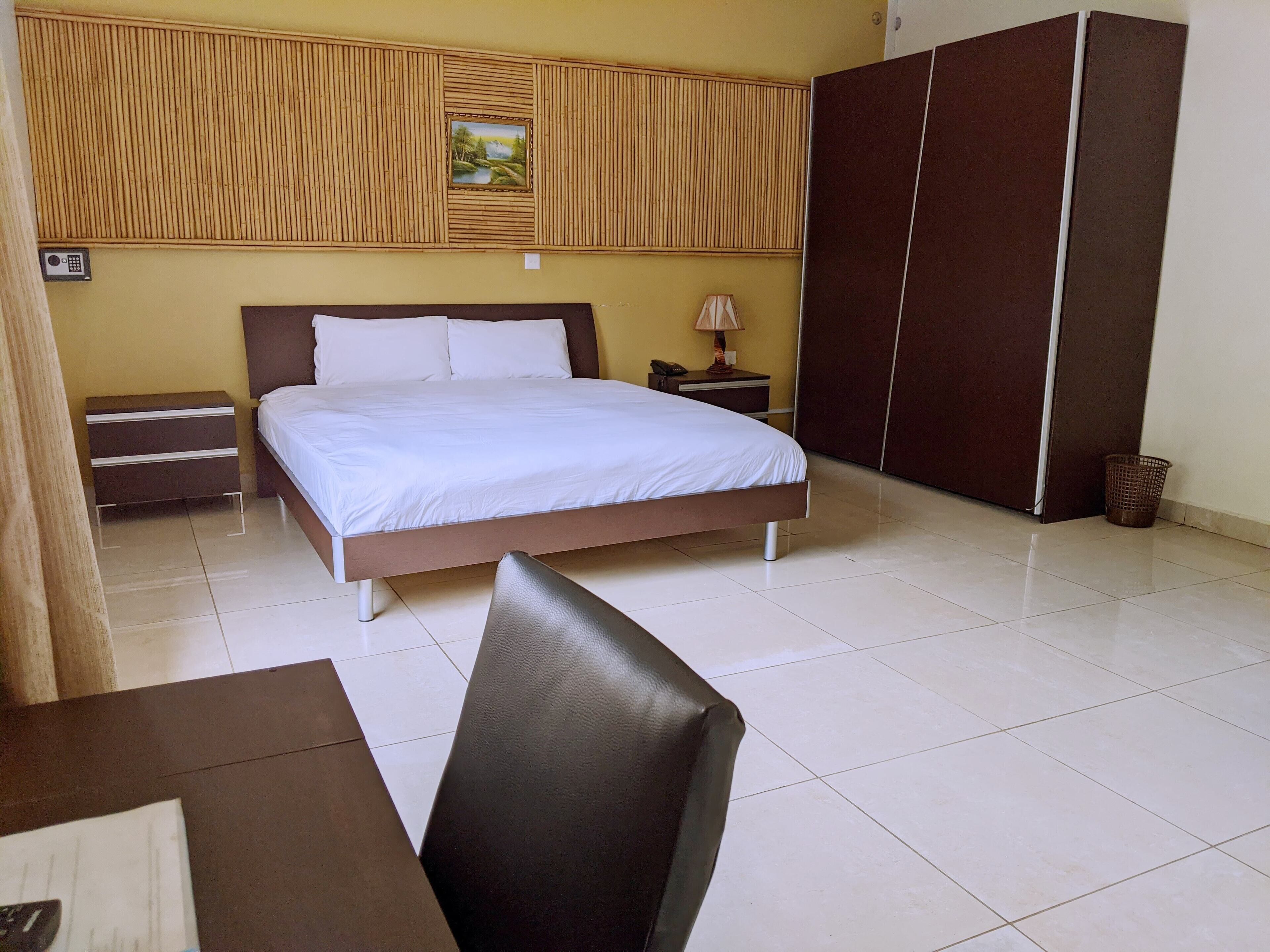 A hotel room with a bed, bedside tables, a lamp, a wardrobe, and a trash bin.