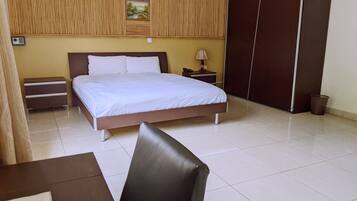 A hotel room with a bed, bedside tables, a lamp, a wardrobe, and a trash bin.