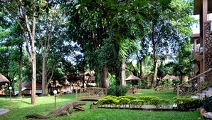 A lush garden with a wooden bridge, a thatched-roof gazebo, and a stone staircase. - Hotel Ruch (Kampala)