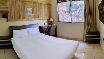 A hotel room with a large bed, a desk with a lamp, a chair, a TV, and a window with curtains.