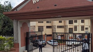 The entrance of Hotel Ruch with a gated driveway, security personnel, and parked cars. - Hotel Ruch (Kampala)