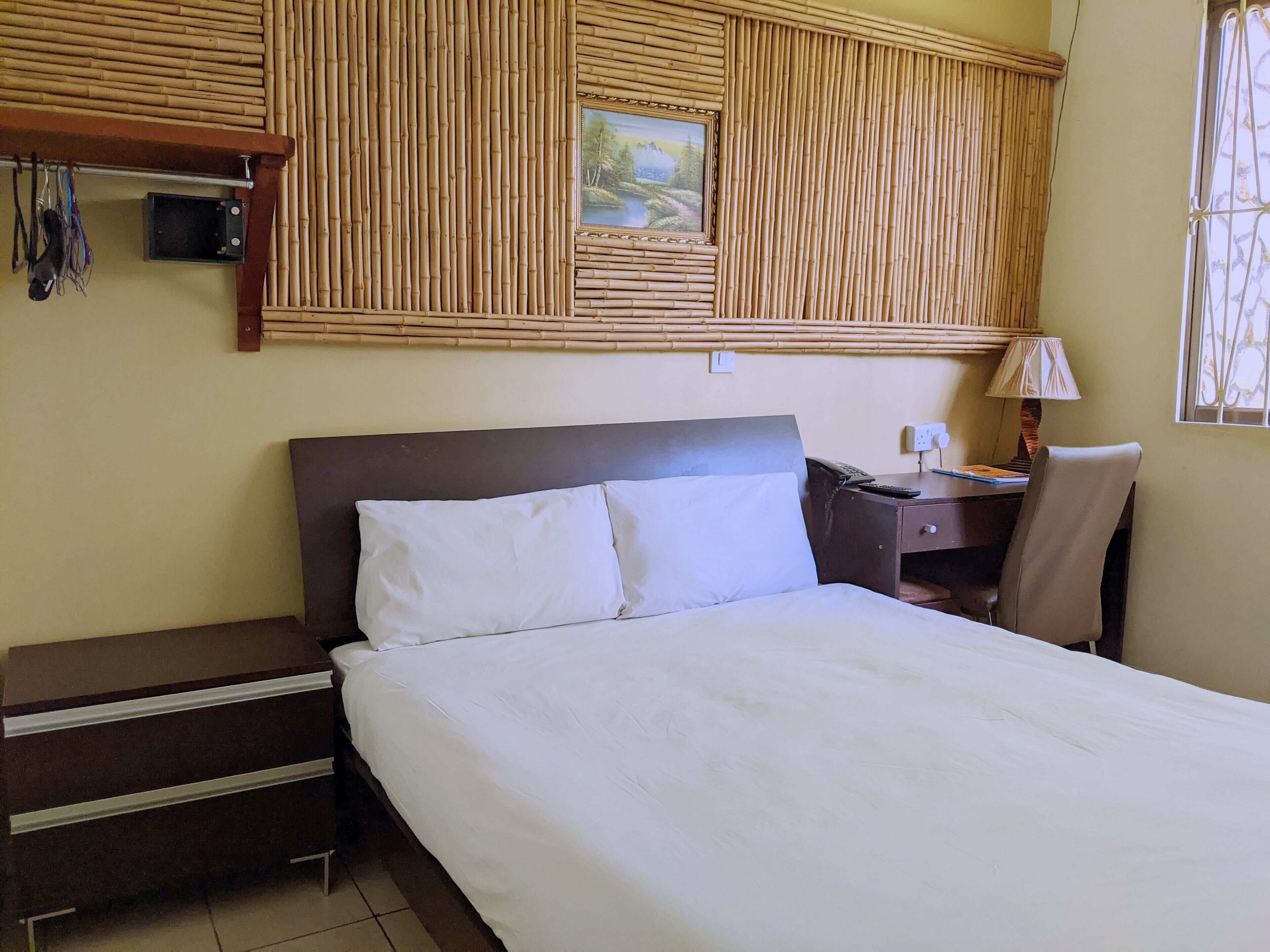 Une chambre d’hôtel avec un lit, un bureau, une chaise, une lampe et un tableau au mur.