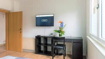 Ett rum med ett skrivbord, en stol, en tv och en krukväxt.