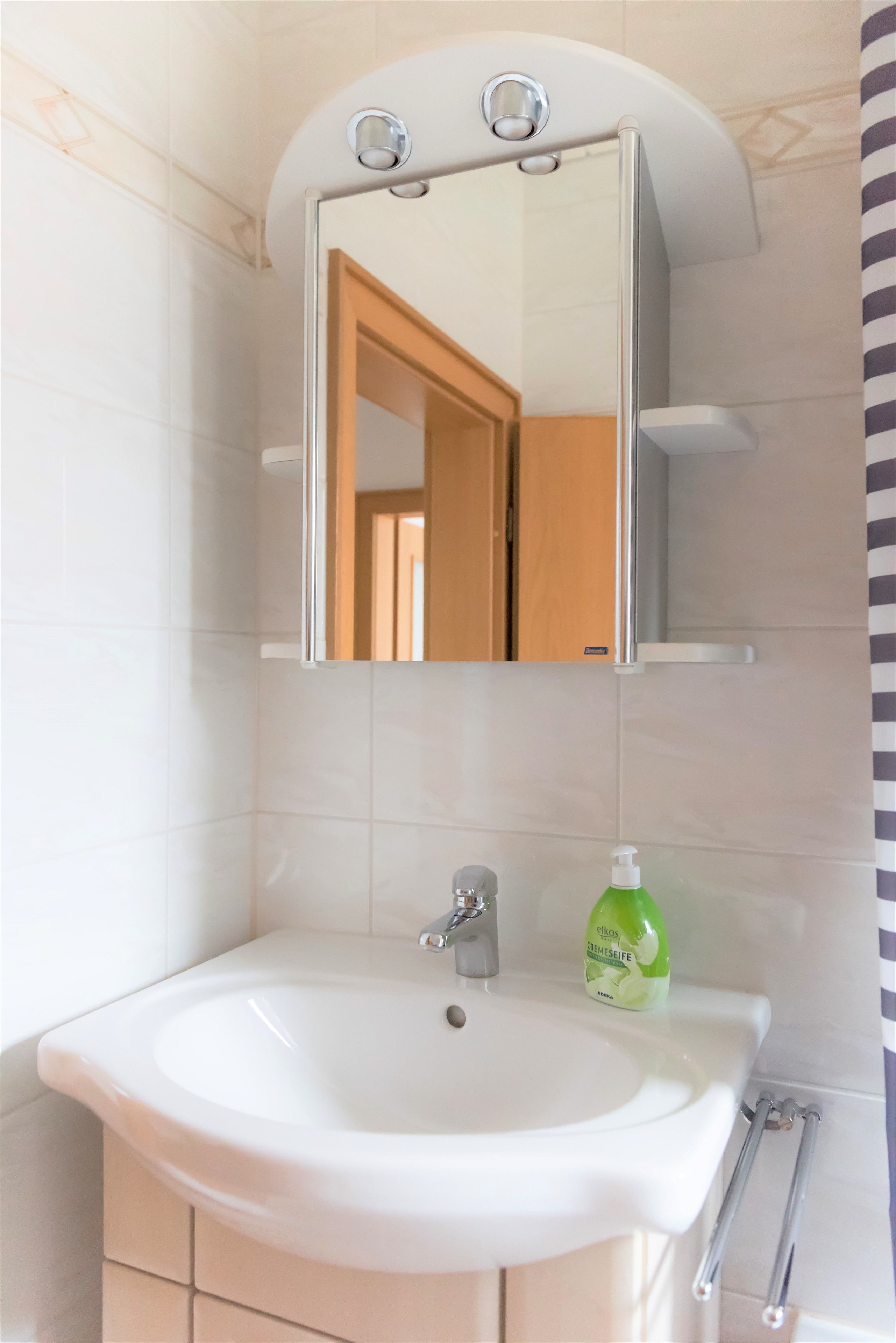 A bathroom with a white sink, a mirror, and a green bottle of soap.