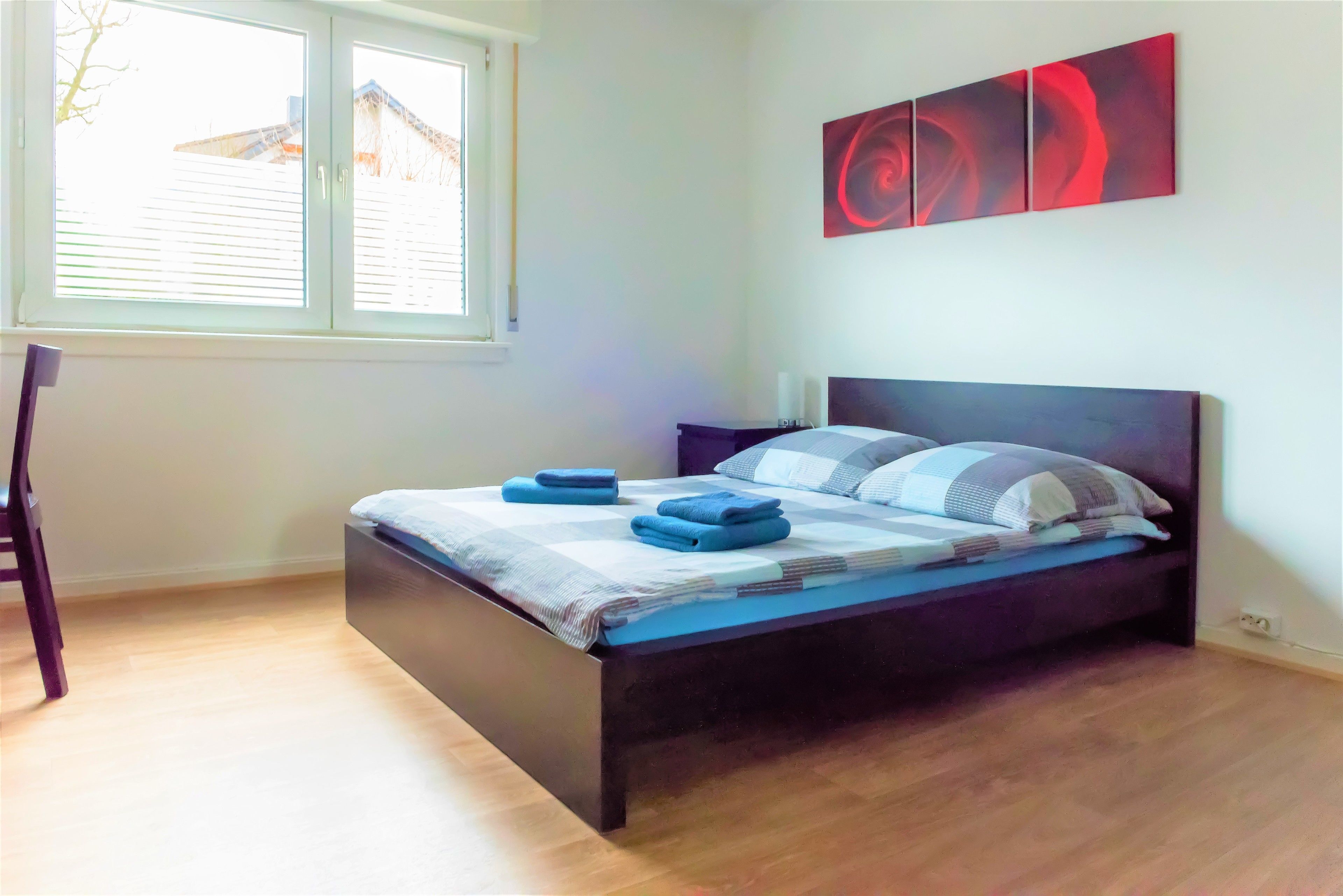 A bedroom with a bed, a window, and a wall-mounted abstract painting.