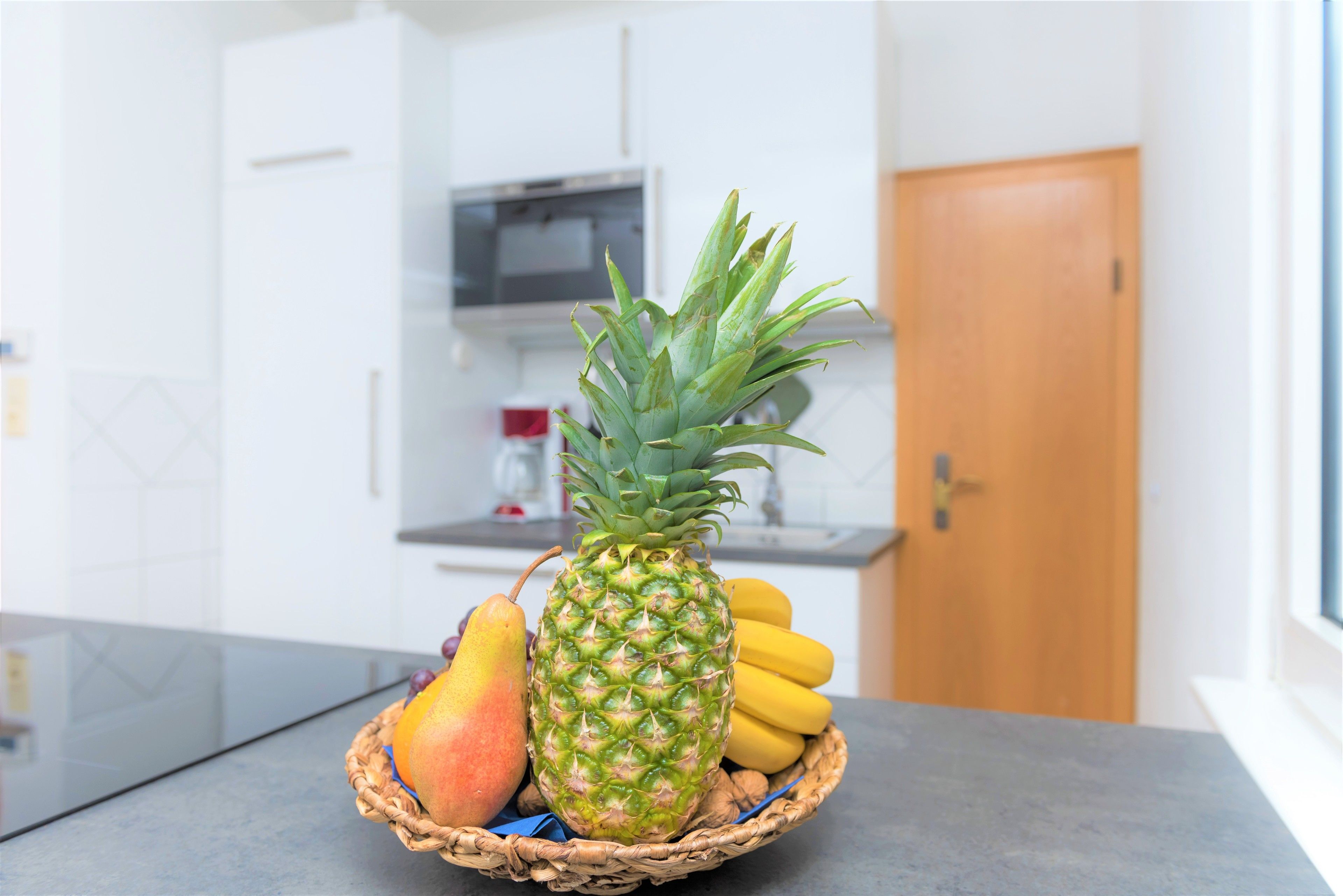 Une cuisine avec un panier de fruits contenant un ananas, des bananes et une mangue, posé sur un plan de travail.