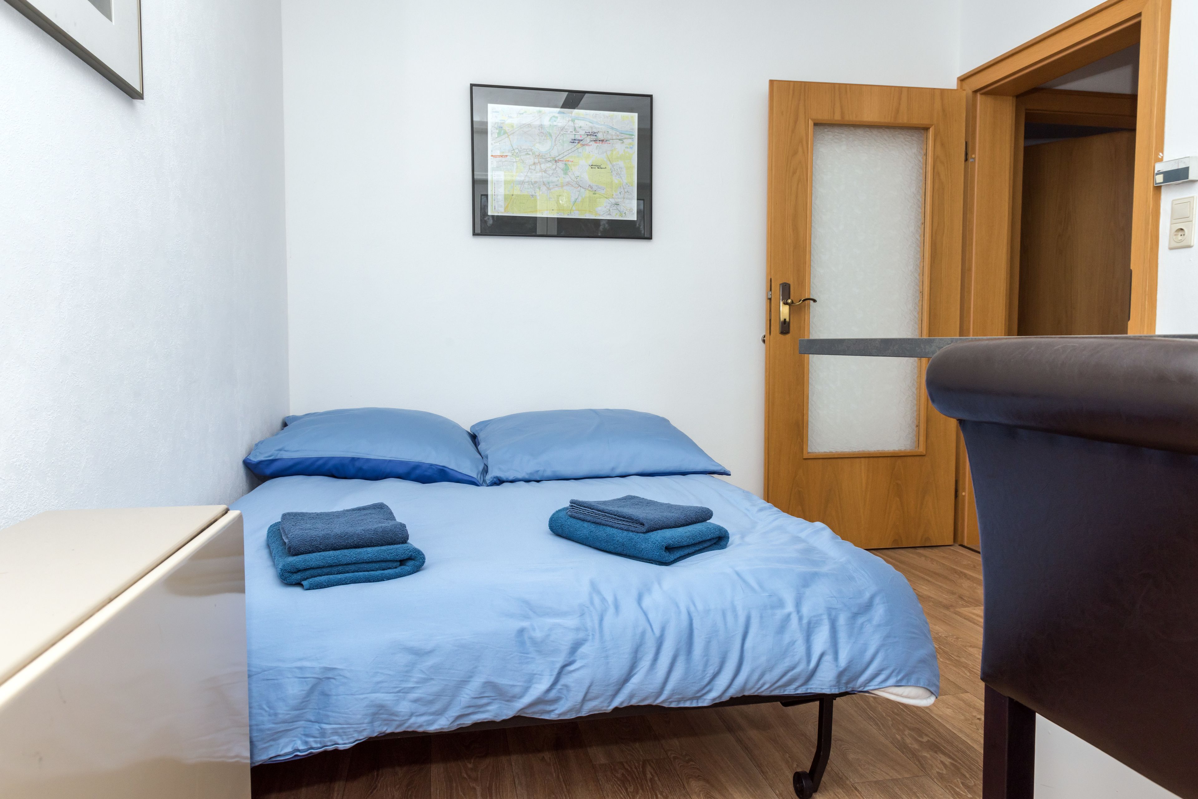 Ein kleiner, ordentlicher Raum mit einem Bett, einem Schreibtisch und einer Tür.