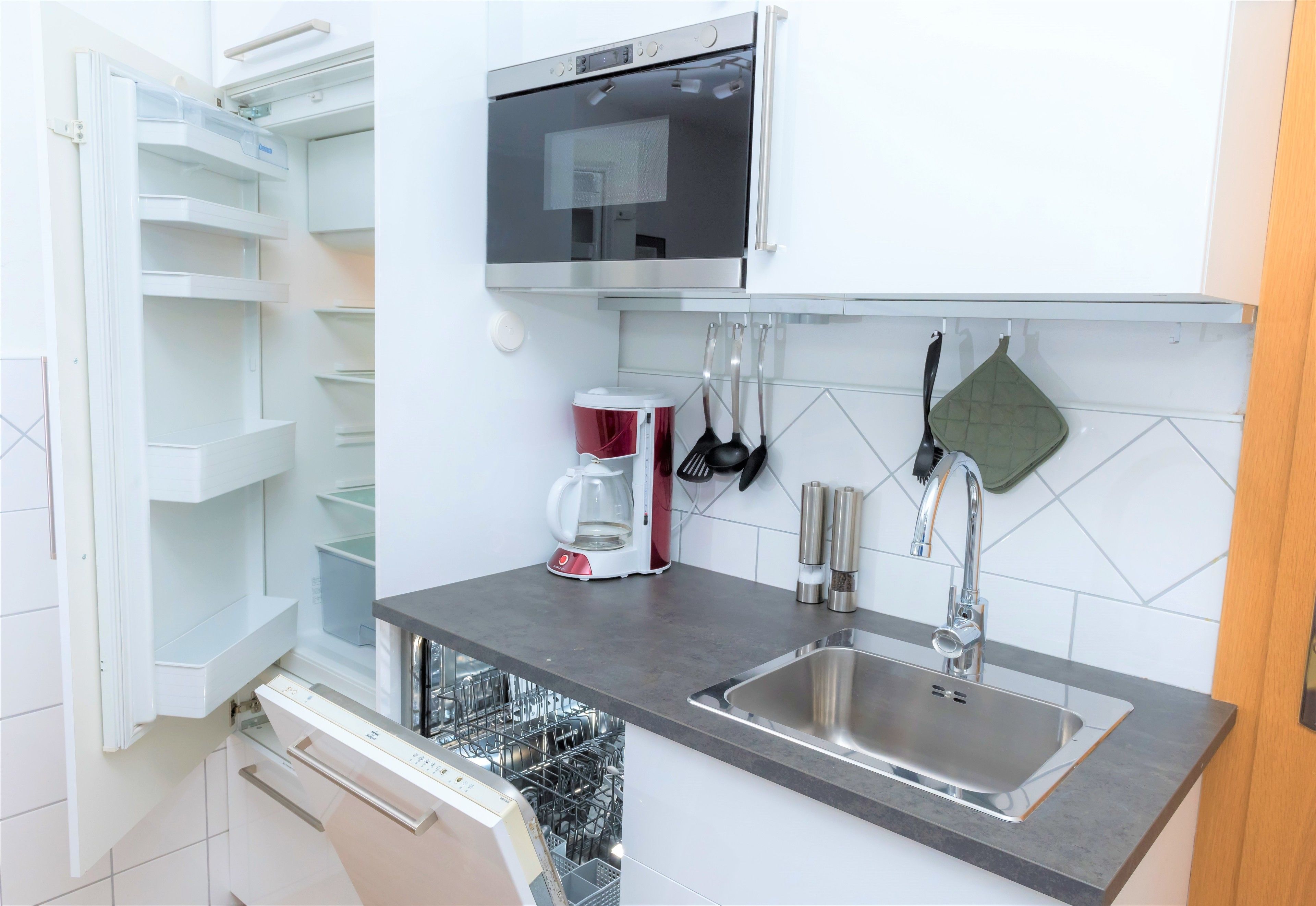 A modern kitchen with a built-in dishwasher, a stainless steel sink, and a microwave above the countertop.