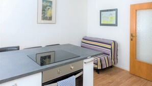 A compact kitchen with a modern design, featuring a built-in stove, a small sink, and a dining area with a striped cushion. - Schaefer Apartments GmbH (Muehlheim am Main)