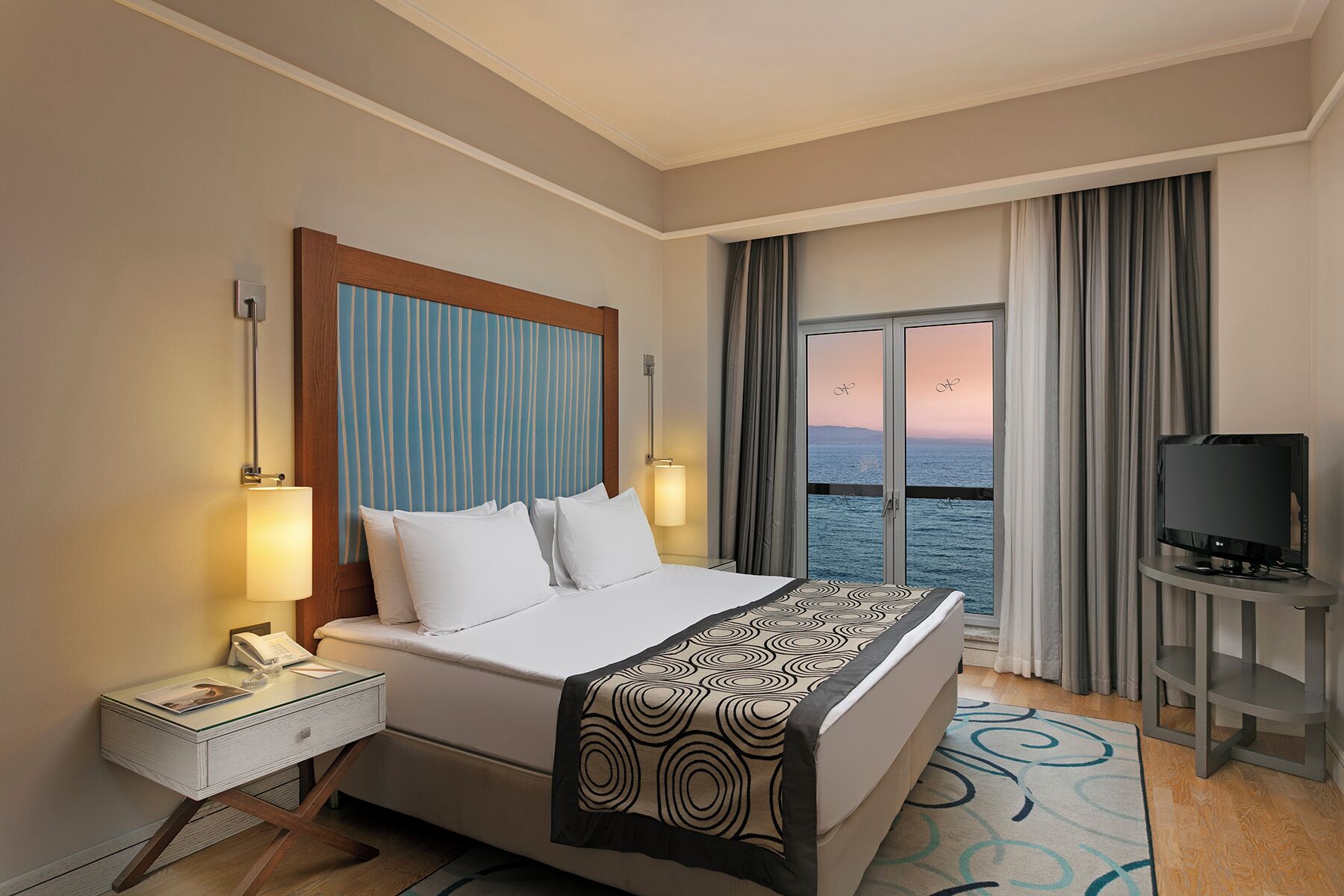 Une chambre d’hôtel avec un lit, une table de chevet avec une lampe, une télévision et une vue sur la mer.
